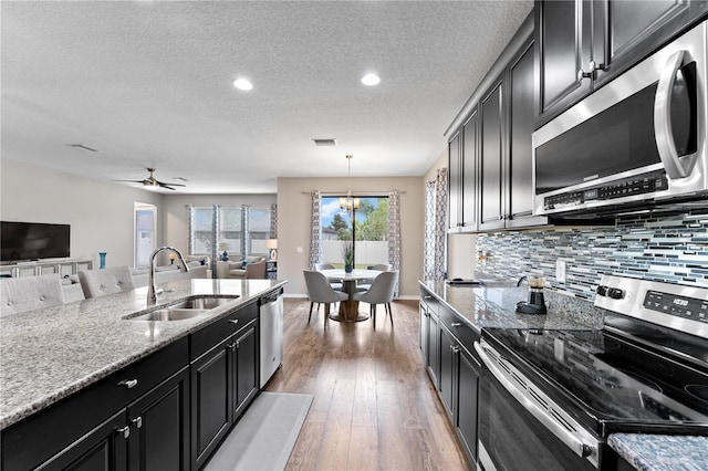 kitchen featuring a sink, wood finished floors, backsplash, dark cabinetry, and appliances with stainless steel finishes