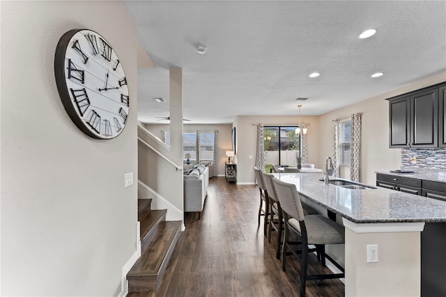 kitchen with an island with sink, a breakfast bar, a sink, dark wood-type flooring, and light stone counters