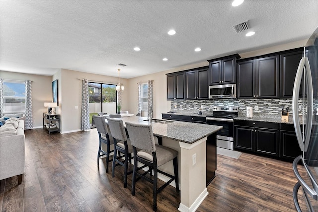 kitchen with dark wood-type flooring, pendant lighting, stainless steel appliances, a center island with sink, and sink