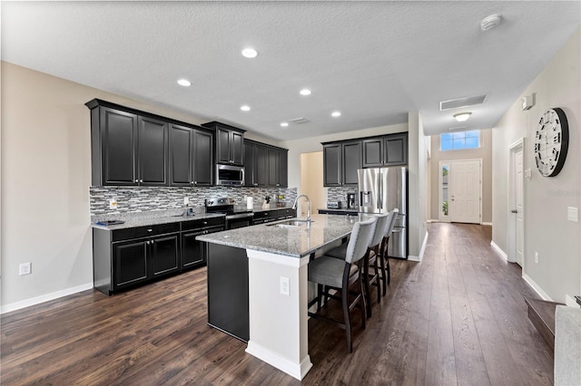 kitchen featuring appliances with stainless steel finishes, a center island with sink, a breakfast bar area, and dark hardwood / wood-style floors