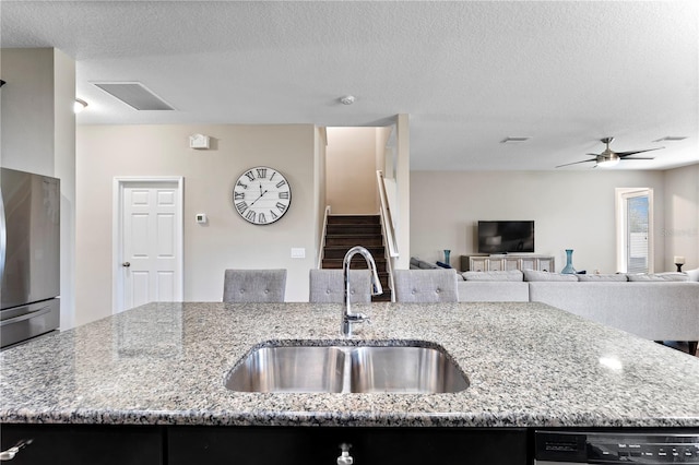 kitchen with a textured ceiling, light stone counters, stainless steel refrigerator, and sink