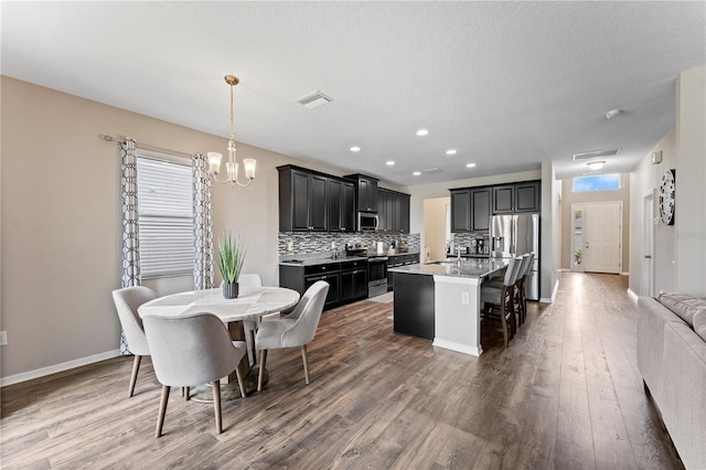 kitchen featuring a sink, a kitchen breakfast bar, dark wood finished floors, appliances with stainless steel finishes, and decorative backsplash