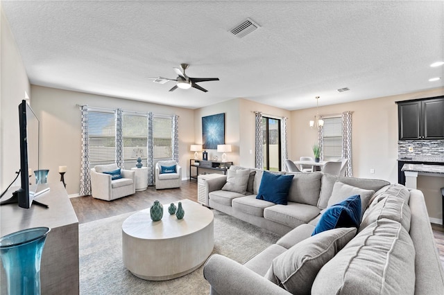 living room with a textured ceiling, ceiling fan with notable chandelier, and light hardwood / wood-style floors