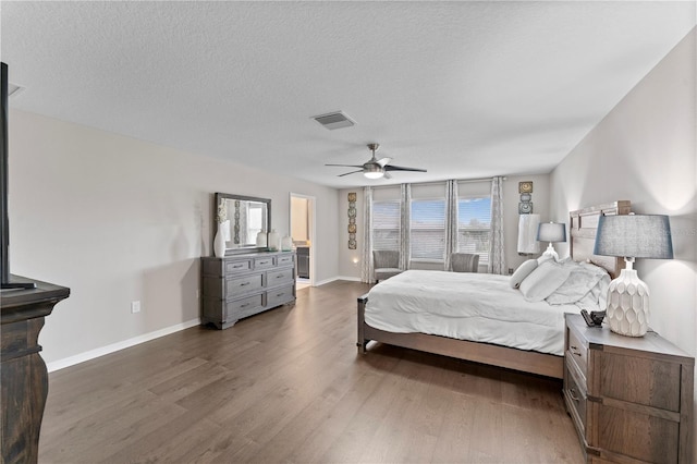 bedroom featuring wood finished floors, a textured ceiling, visible vents, baseboards, and ceiling fan