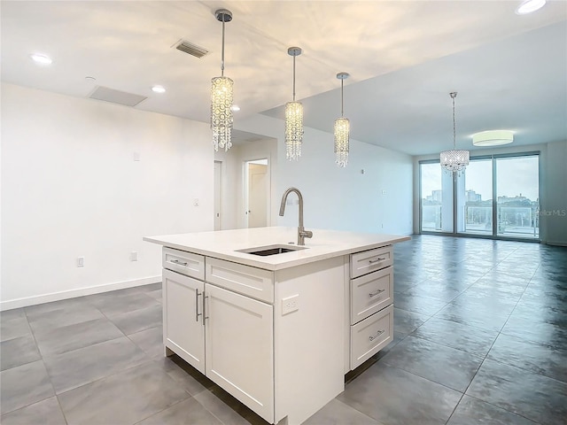 kitchen with white cabinets, decorative light fixtures, a wall of windows, an island with sink, and sink