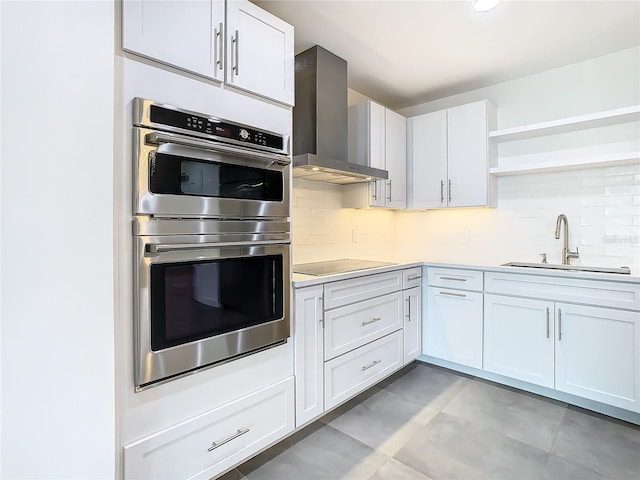 kitchen with stainless steel double oven, sink, white cabinets, wall chimney exhaust hood, and black electric cooktop