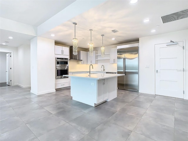 kitchen featuring white cabinets, appliances with stainless steel finishes, sink, hanging light fixtures, and a center island with sink