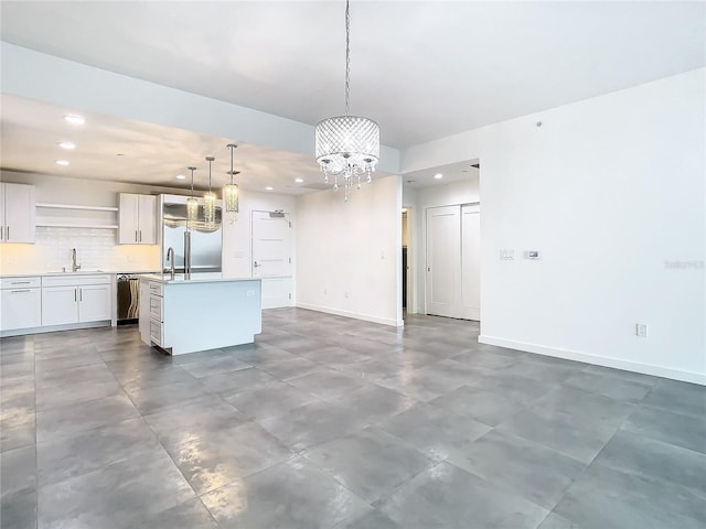 kitchen with pendant lighting, white cabinetry, appliances with stainless steel finishes, an island with sink, and a chandelier