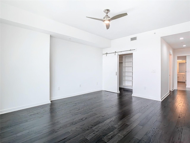 empty room featuring ceiling fan, a barn door, and dark hardwood / wood-style floors