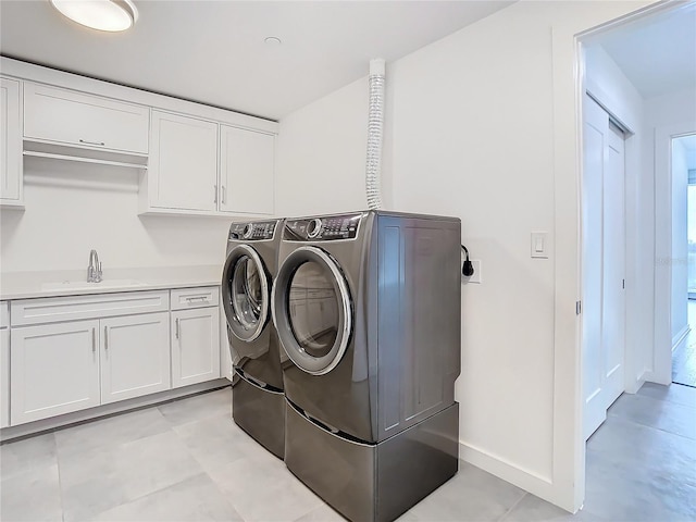 clothes washing area with cabinets, washing machine and clothes dryer, and sink