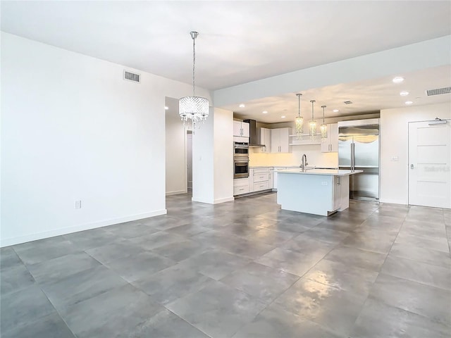 kitchen featuring pendant lighting, white cabinetry, stainless steel appliances, a kitchen island with sink, and a chandelier