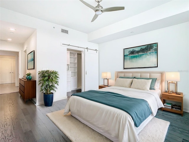 bedroom featuring ceiling fan, wood-type flooring, a spacious closet, and a barn door