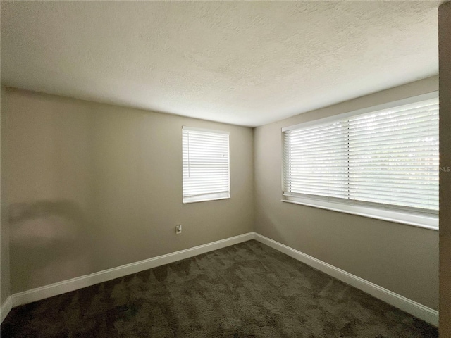 spare room with a textured ceiling, dark colored carpet, and a wealth of natural light