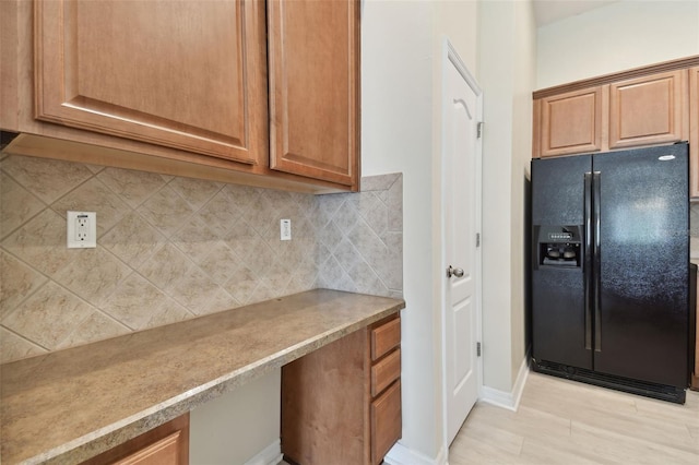 kitchen with black refrigerator with ice dispenser, built in desk, backsplash, and light hardwood / wood-style floors