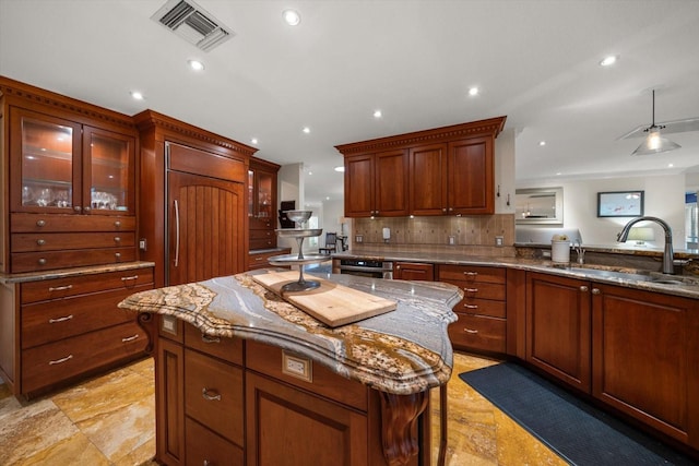 kitchen featuring light stone countertops, paneled fridge, a kitchen island, and sink