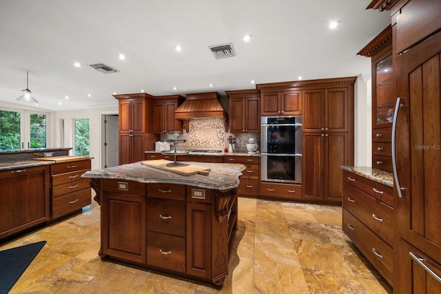 kitchen with premium range hood, decorative backsplash, appliances with stainless steel finishes, a kitchen island, and light stone counters