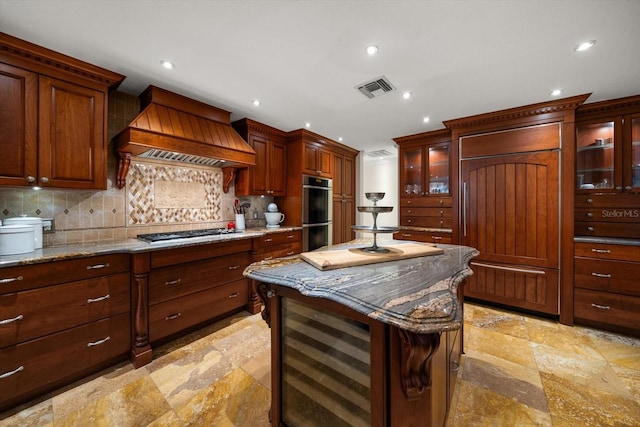 kitchen featuring light stone countertops, a center island, stainless steel appliances, decorative backsplash, and custom range hood