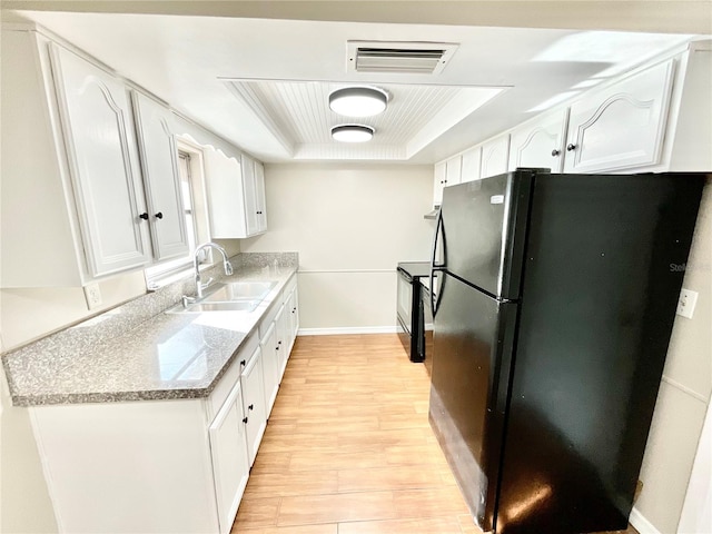 kitchen featuring light stone counters, white cabinets, black appliances, a tray ceiling, and light wood-type flooring