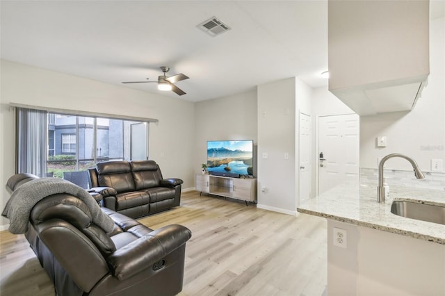 living room featuring light wood-type flooring, ceiling fan, and sink