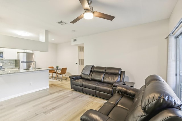 living room featuring ceiling fan, light wood-type flooring, and sink