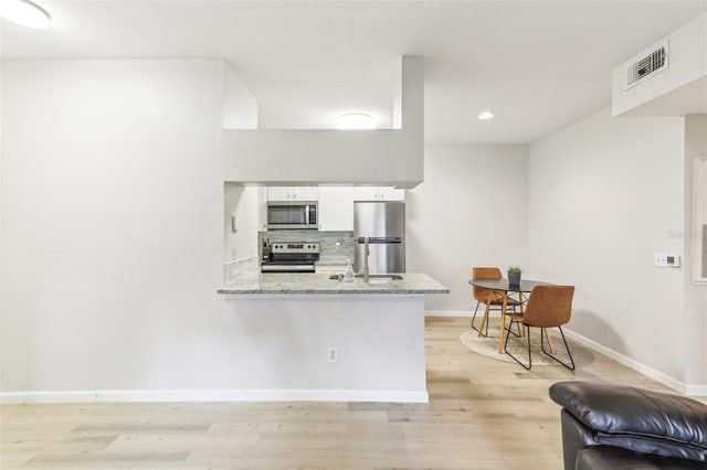 kitchen featuring kitchen peninsula, white cabinetry, stainless steel appliances, light stone countertops, and light hardwood / wood-style floors