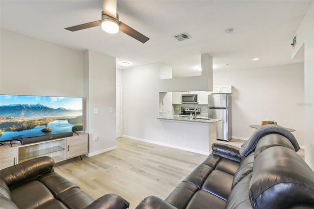 living room with light hardwood / wood-style floors, ceiling fan, and sink