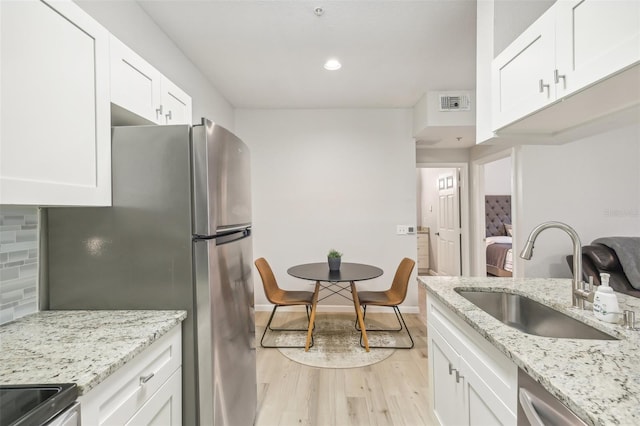 kitchen featuring sink, white cabinetry, appliances with stainless steel finishes, light wood-type flooring, and decorative backsplash