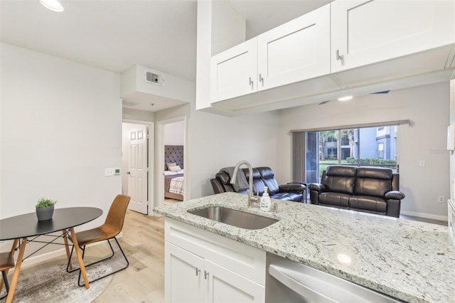 kitchen with light stone counters, light hardwood / wood-style floors, sink, and white cabinetry