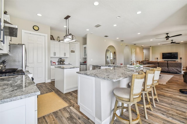 kitchen featuring a spacious island, light stone countertops, pendant lighting, white cabinets, and ceiling fan