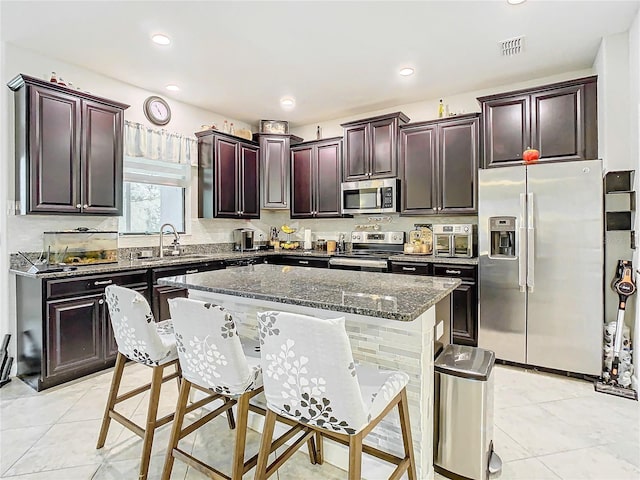 kitchen with visible vents, appliances with stainless steel finishes, a breakfast bar, dark stone countertops, and a sink