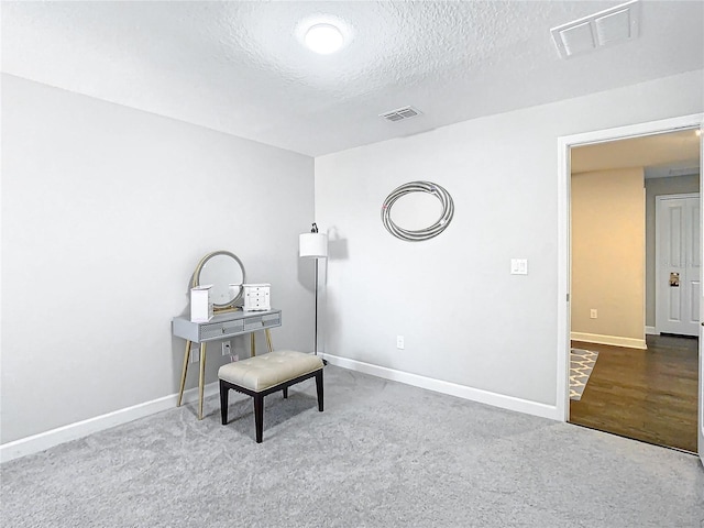 living area with carpet flooring, visible vents, a textured ceiling, and baseboards