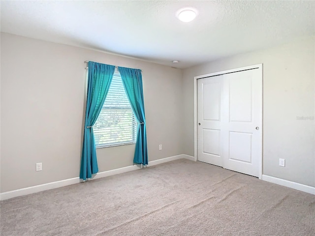 unfurnished bedroom with a closet, carpet flooring, a textured ceiling, and baseboards