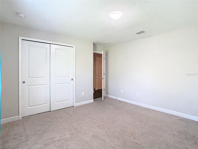 unfurnished bedroom with a closet, visible vents, light carpet, and baseboards