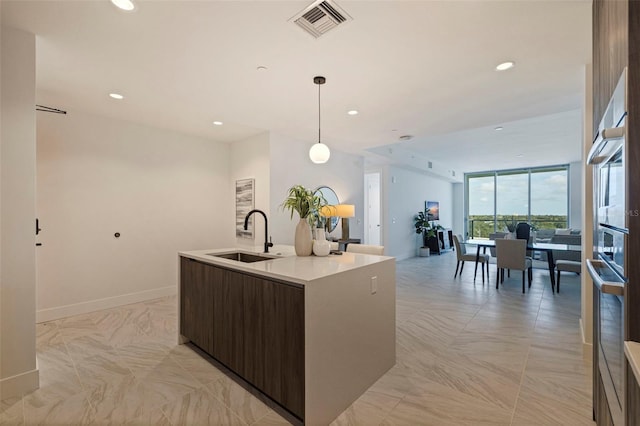 kitchen featuring pendant lighting, a center island with sink, expansive windows, sink, and dark brown cabinets