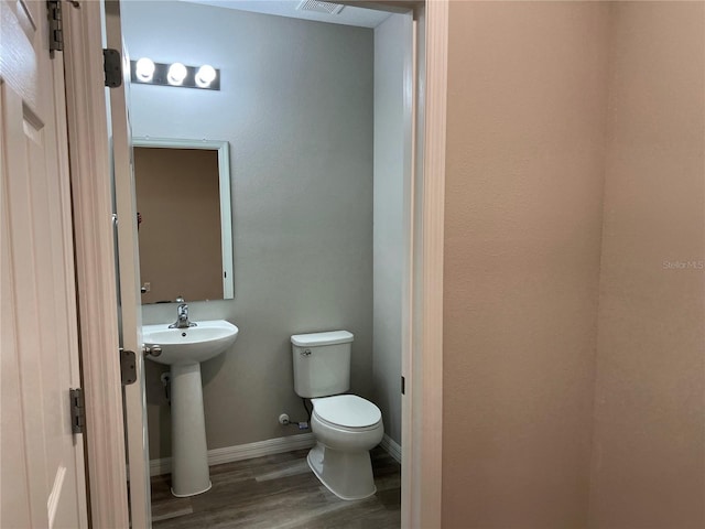 half bath featuring visible vents, baseboards, a sink, toilet, and wood finished floors