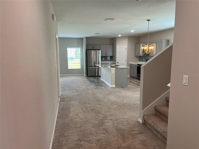 hall with a sink, baseboards, an inviting chandelier, and light colored carpet
