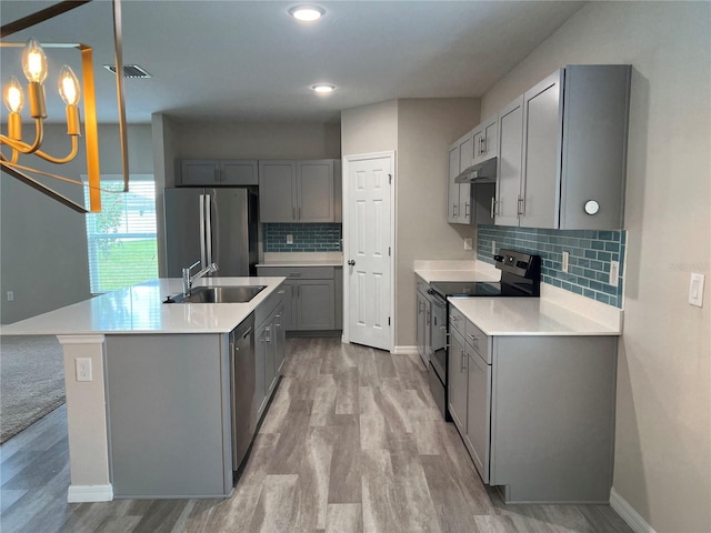 kitchen featuring under cabinet range hood, a sink, stainless steel appliances, light wood finished floors, and gray cabinetry