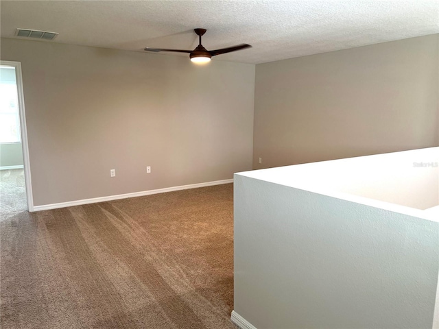 carpeted empty room featuring visible vents, ceiling fan, baseboards, and a textured ceiling