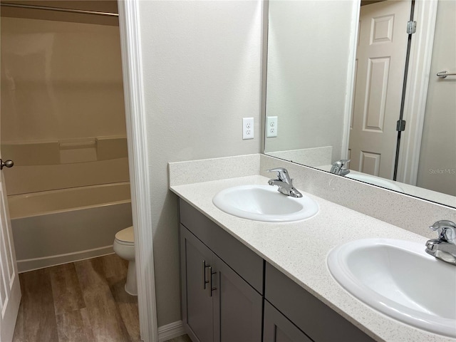 full bath featuring toilet, wood finished floors, double vanity, and a sink
