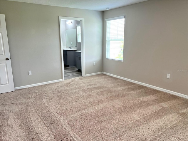 unfurnished bedroom with ensuite bath, baseboards, and light colored carpet