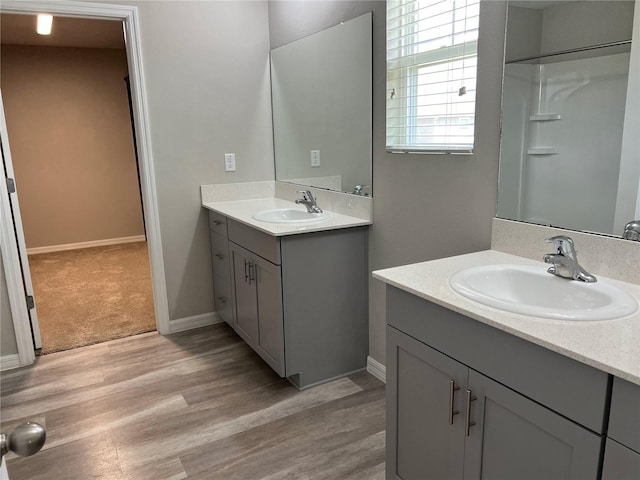 bathroom featuring two vanities, wood finished floors, a sink, and baseboards