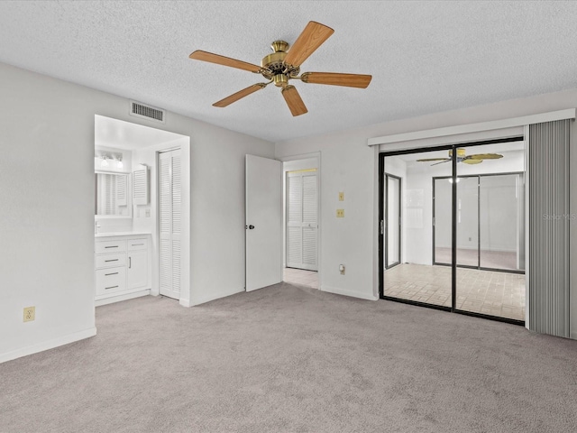 unfurnished bedroom with a textured ceiling, ensuite bathroom, ceiling fan, and light colored carpet