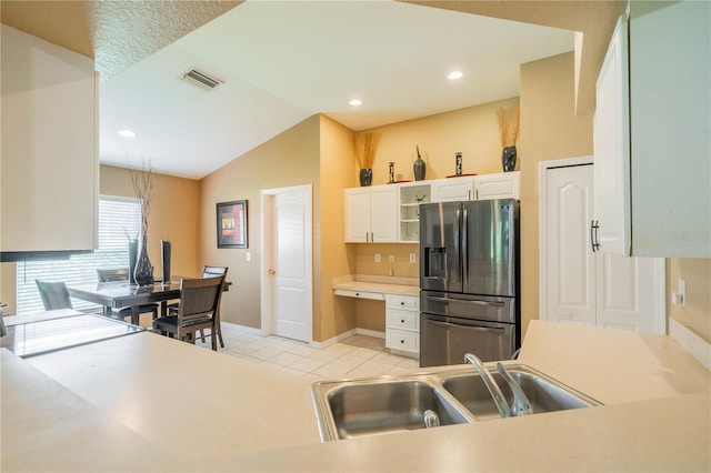 kitchen with white cabinets, light tile patterned floors, sink, stainless steel refrigerator with ice dispenser, and vaulted ceiling