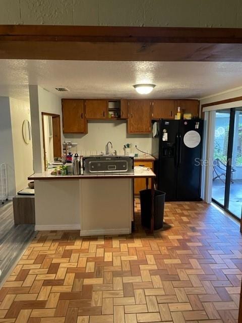 kitchen featuring light parquet floors, kitchen peninsula, and black fridge