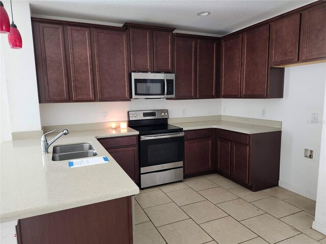 kitchen featuring stainless steel appliances, sink, light tile patterned flooring, pendant lighting, and a textured ceiling