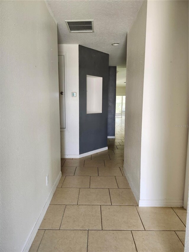 hall with a textured ceiling and light tile patterned floors