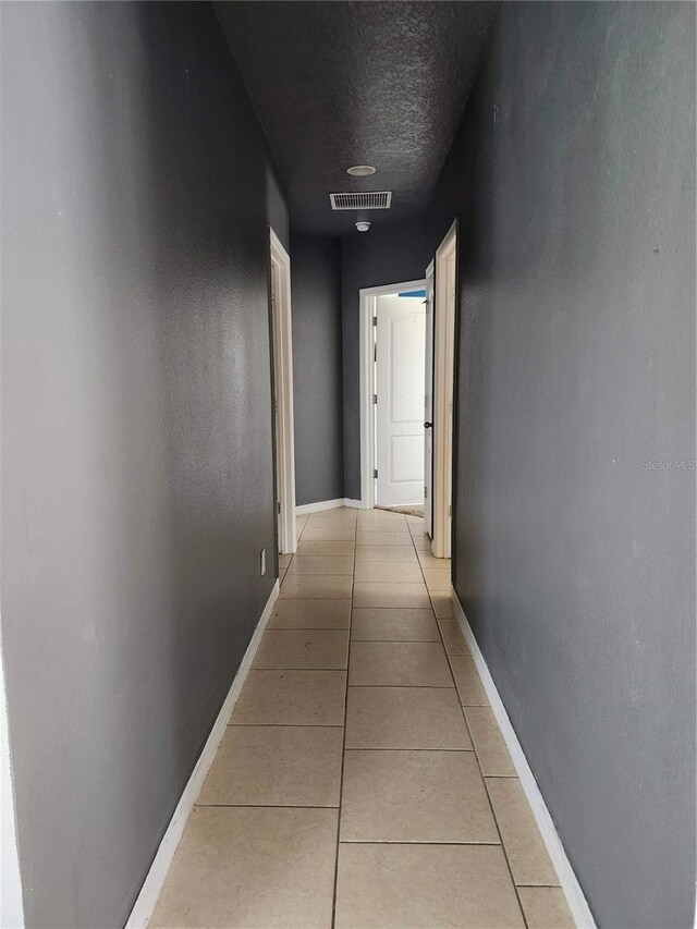 hall with a textured ceiling and light tile patterned floors