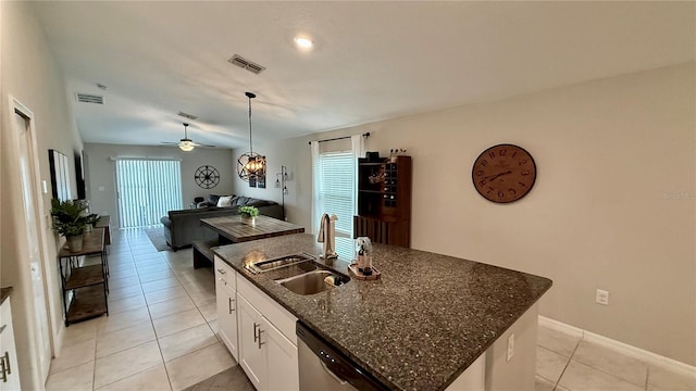 kitchen featuring dark stone counters, a kitchen island with sink, sink, white cabinetry, and decorative light fixtures