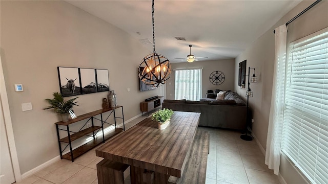 dining room featuring ceiling fan with notable chandelier, a wealth of natural light, vaulted ceiling, and light tile patterned flooring