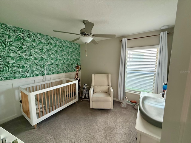 bedroom featuring carpet floors, ceiling fan, and a nursery area